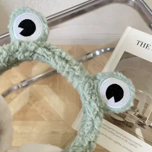 Close-up view of cute green plush frog earmuffs with embroidered eyes and soft fluffy texture