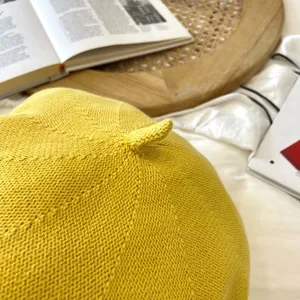 Detailed view of the fine knitting texture and decorative top stem of a yellow painter beret