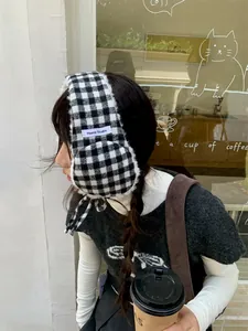 Lifestyle detail of a woman wearing black and white plaid plush earmuffs in a cafe setting