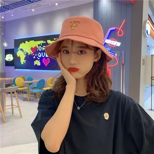 Cute pink bucket hat with potato embroidery worn by a model in a vibrant cafe setting.