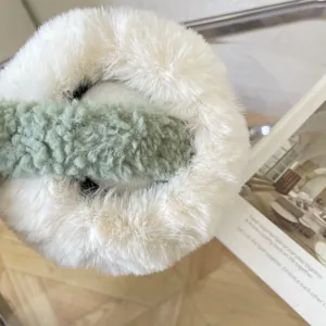 Macro view of the soft white faux fur and green textured fabric of the plush earmuffs
