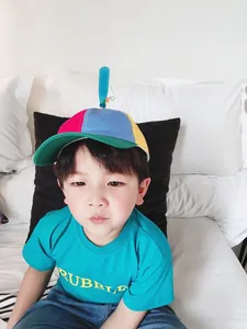Close-up of a child wearing a colorful propeller baseball cap in a home setting
