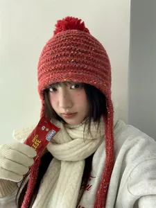 Close-up of a terracotta knitted beanie with a pom-pom and ear flaps worn by a model