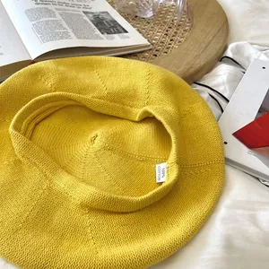 Detail view of yellow knitted beret hat showing 100% cotton tag and fine knit texture