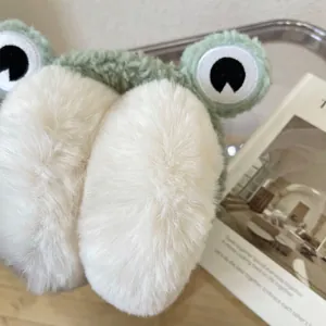 Macro view of cute green frog plush winter earmuffs with soft white faux fur texture