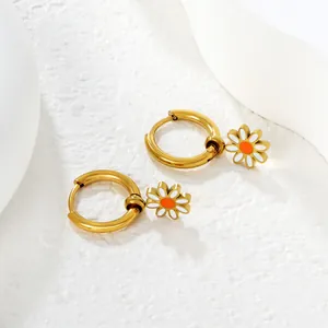 Close-up of gold stainless steel hoop earrings featuring white and orange daisy charms