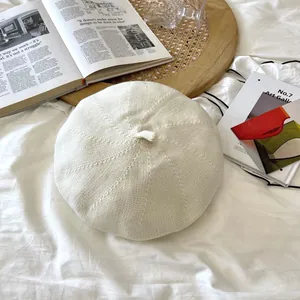 Close-up macro view of a breathable off-white knitted beret hat with detailed stitch patterns