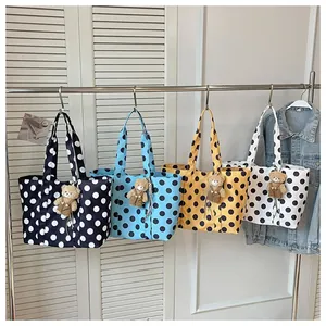 Detailed view of four colorful polka dot tote bags with teddy bear charms on a rack.