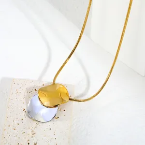 Gros plan d'un collier chaîne serpent dorée avec un pendentif disque irrégulier bicolore