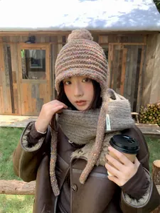 Model wearing a cozy brown knitted beanie with colorful flecks and ear flaps outdoors.