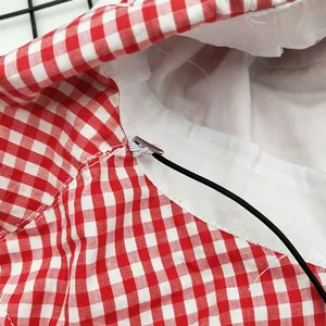 Dettaglio del cordino sottogola nero regolabile attaccato a un cappello a quadretti rossi.