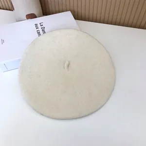 Detailed top view of a cream wool beret hat placed on a white desk with aesthetic book