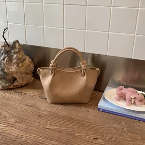Vintage tan textured leather bucket bag with knotted handles on wooden table