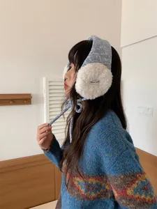 Gros plan d'une femme portant des cache-oreilles en tricot bleu et peluche blanche.