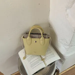 Vue détaillée d'un mini sac à main seau jaune avec doublure à cordon rayée et logo