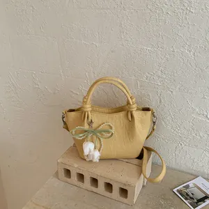 Vintage yellow bucket shoulder bag with elegant pearl flower bow charm on a stone block.