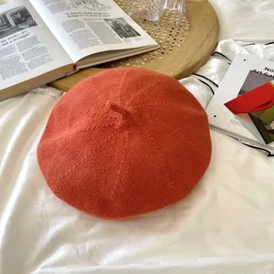 Detail shot of orange knitted beret hat showing breathable texture and top stem.
