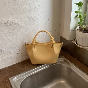 Detailed macro view of a trendy yellow solid color bucket bag with unique knot handle design