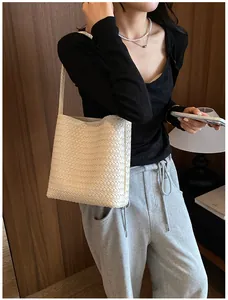 Detalle de estilo de un bolso de cubo tejido crema llevado al hombro por una modelo.