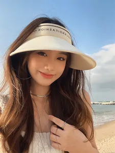 Gros plan d'une femme portant une visière pare-soleil élégante à large bord à la plage.