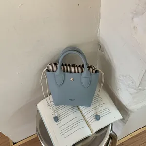 Mini sac à main en cuir bleu ciel avec doublure à rayures posé sur un livre ancien