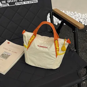 Detailed view of cream grid pattern gym bag with orange handles on a chair