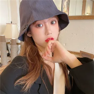 Detail shot of a woman wearing a pleated dark grey bucket hat in a cafe setting