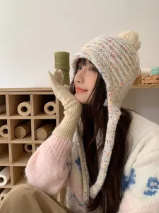 Side view of woman wearing candy-colored knit beanie with ear flaps and pom-pom