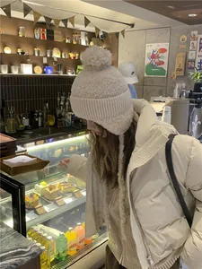 Vrouw draagt dikke crème gebreide muts met witte pompon in een gezellige café-omgeving