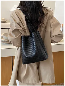 Bolso de hombro tipo cubo tejido en negro minimalista mostrado en un modelo elegante