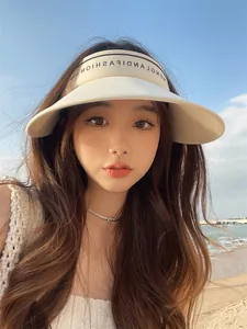 Belle femme asiatique portant un pare-soleil beige élégant à large bord sur une plage