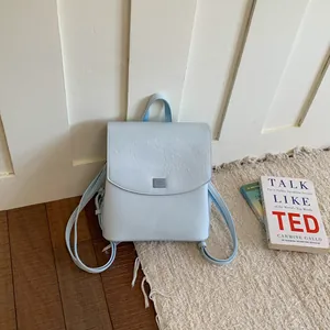 Minimalist light blue backpack with textured finish and slim straps in lifestyle setting.