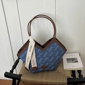 Detailansicht einer blauen Denim-Tragetasche mit braunem Lederbesatz und Griffen