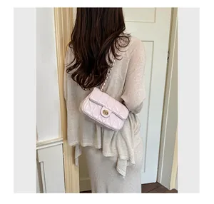 Detailopname van een roze gewatteerde kettingtas gedragen bij een beige outfit.