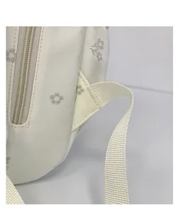 Macro detail of a white student backpack showing floral pattern, zipper, and strap stitching