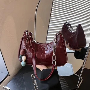 Close-up of burgundy crocodile embossed shoulder bag with silver chain and charm