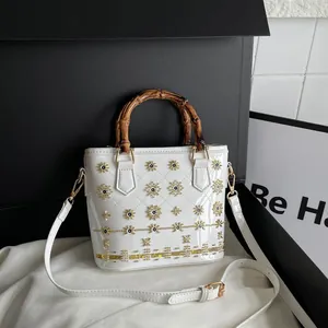 Elegant white quilted bucket bag featuring a natural bamboo handle and gold floral embroidery.