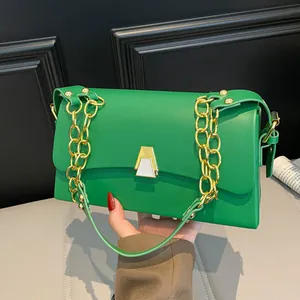 Detailed view of vibrant green fashion handbag with gold chain strap held by hand