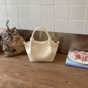 Detailed view of cream textured leather bucket bag with knotted handles on rustic wooden surface