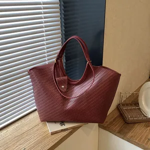 Close-up of large burgundy woven tote bag showing detailed cross-weave texture.
