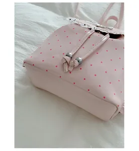 Close-up of pink polka dot backpack with lace trim and bow detail on a white background.