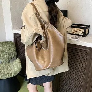 Side view of a large brown slouchy faux leather tote bag worn by a model in a room.