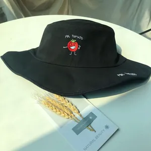 Close-up detail of a cute smiling tomato embroidery on a black flat-top sun bucket hat.