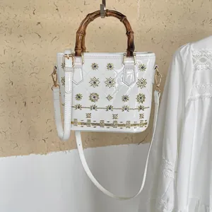Close-up of white patent leather bucket bag with bamboo handle and floral beadwork