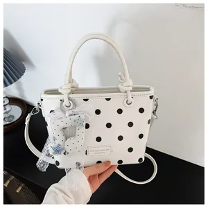 Detailed shot of a trendy white handbag featuring black polka dots and a cute lace charm