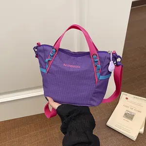 Hand holding a purple grid pattern tote bag with vibrant pink and blue stylish straps