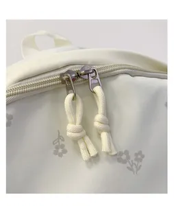 Close-up detail of white floral backpack with double metal zipper and rope pulls