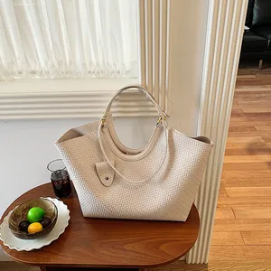 Close-up of a stylish beige woven tote bag displayed on a wooden table in a bright room
