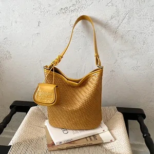 Yellow woven bucket shoulder bag with small pouch displayed on books and chair