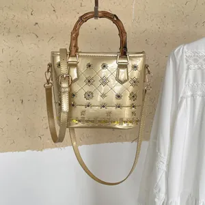 Metallic gold quilted bucket bag featuring elegant bamboo handles and floral studs
